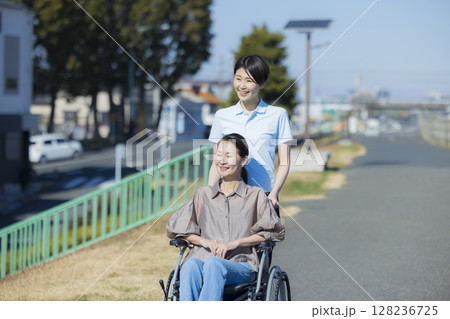 車椅子に乗る女性を押す女性介護士 車椅子に乗る女性を押す女性介護士 128236725