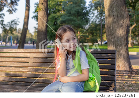 Young girl with backpack using smartphone on park bench Young girl with backpack using smartphone on park bench 128237261