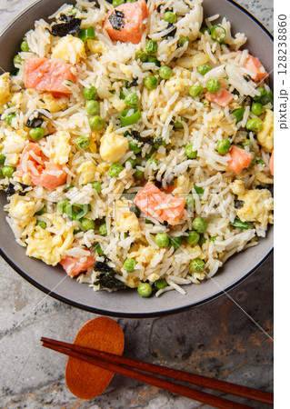 Asian fried rice with red fish, seaweed, green peas, onion and omelet close-up in a bowl on the table. Vertical top view 128238860