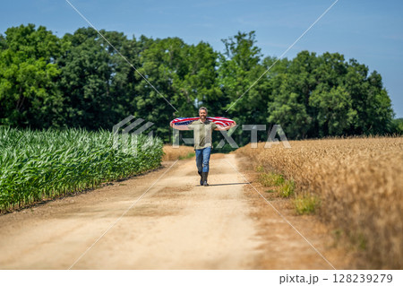 Man with American flag in crop field. Independence day of America. 4th of July. American Flag for labor Day or 4th of July. American flag and man farmer. Flag of the USA. Independence day Man with American flag in crop field. Independence day of America. 4th of July. American Flag for labor Day or 4th of July. American flag and man farmer. Flag of the USA. Independence day 128239279