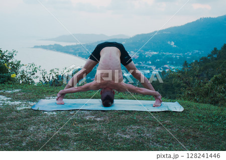 A Male Yogi Engaging in the Practice of an Advanced Yoga Pose in a Beautiful Outdoor Setting A Male Yogi Engaging in the Practice of an Advanced Yoga Pose in a Beautiful Outdoor Setting 128241446