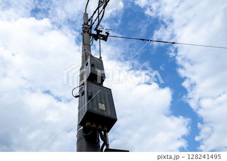 Towering utility pole supporting multiple electrical boxes and complex power lines against a vast, vibrant blue sky, symbolizing modern urban infrastructure Towering utility pole supporting multiple electrical boxes and complex power lines against a vast, vibrant blue sky, symbolizing modern urban infrastructure 128241495