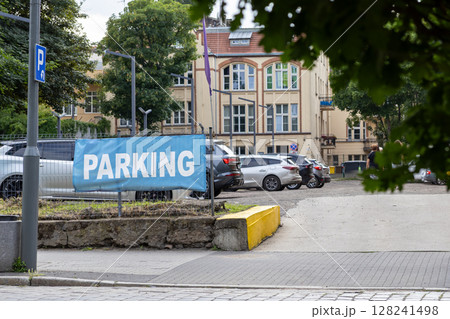 Blue banner displaying PARKING text clearly positioned at the entrance of an outdoor car lot, offering available space for vehicles in a busy urban area Blue banner displaying PARKING text clearly positioned at the entrance of an outdoor car lot, offering available space for vehicles in a busy urban area 128241498