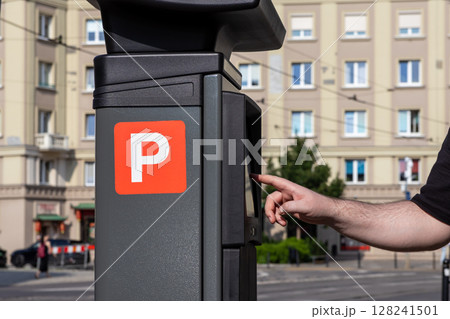A person's hand operates a modern parking meter, featuring a prominent 'P' symbol, for efficient city parking payment in an urban environment 128241501