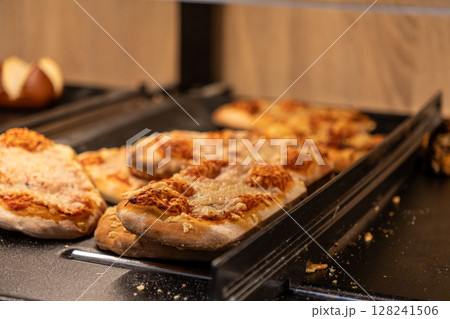 Freshly baked small pizzas with melted cheese and savory tomato sauce displayed on a buffet tray, offering a convenient grab-and-go snack or quick meal Freshly baked small pizzas with melted cheese and savory tomato sauce displayed on a buffet tray, offering a convenient grab-and-go snack or quick meal 128241506