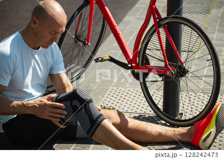 Cyclist fell off his bike and injured his knee. Unhappy cyclist with knee pain and injury outdoors. Close up. Cyclist fell off his bike and injured his knee. Unhappy cyclist with knee pain and injury outdoors. Close up. 128242473
