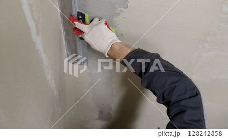 Construction worker applying plaster on wall with spatula Construction worker applying plaster on wall with spatula 128242858