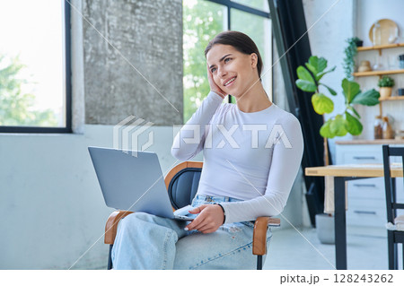 Young teenage girl using laptop for video chat sitting on chair at home 128243262