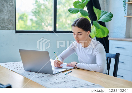 Teenage girl student sitting at the table with laptop, textbooks in home interior 128243264