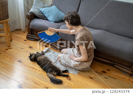 Sweltering heat and stuffy air in apartment. Female using handheld fan to cool animal pet at home Sweltering heat and stuffy air in apartment. Female using handheld fan to cool animal pet at home 128243374