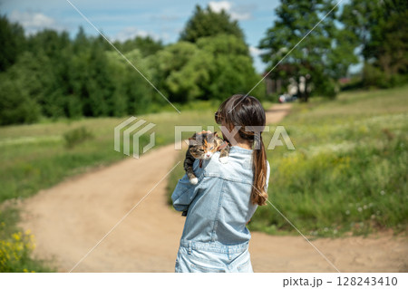 Rear view of woman hugging calm peaceful cat tightly while walking in rural countryside nature area 128243410