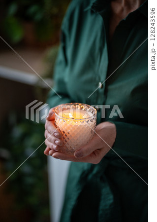 Lit fragrant candle in woman hands, flickering flame. Stress relief, quiet introspection, meditation Lit fragrant candle in woman hands, flickering flame. Stress relief, quiet introspection, meditation 128243596