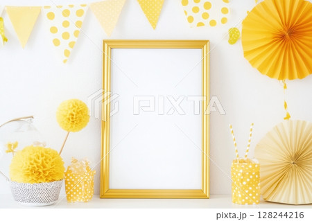 Vertical golden frame on white wall with festive yellow paper decorations, polka dot bunting and party elements. Bright and cheerful celebration mockup for birthday or event design. Copy space 128244216
