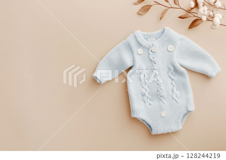 Baby knitted onesie on beige background. Fashion newborn clothes. Flat lay top view. Wool kid soft clothing. Infant trendy bodysuit made of organic eco friendly cotton. Children wardrobe. Baby garment 128244219