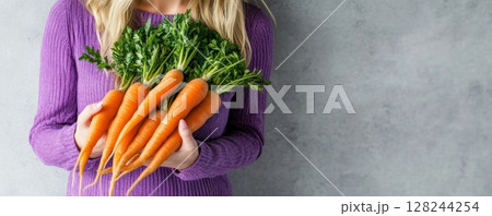 Freshly picked carrots with green tops in hands. Vibrant orange color, healthy and organic vegetables in a natural garden setting. Perfect image for farm food, health, nutrition and lifestyle. Banner 128244254