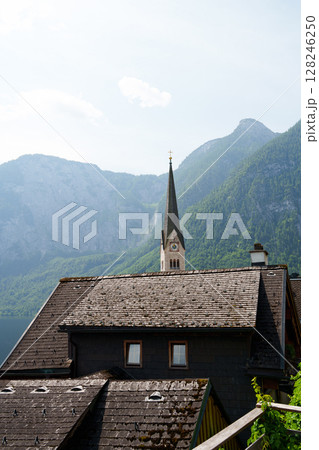A church in Hallstatt against the backdrop of mountains and a lake. Roofs of houses are in the foreground. 128246250