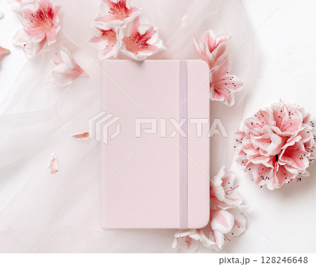 Blank vertical paper card near pink azalea flowers and ribbons top view, spring wedding mockup 128246648
