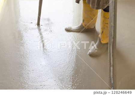 Worker wearing yellow rubber boots pouring concrete over floor in a new house construction site. Worker wearing yellow rubber boots pouring concrete over floor in a new house construction site. 128246649