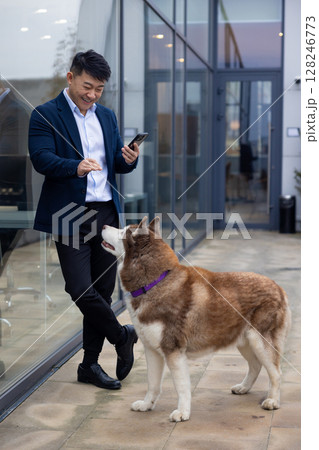 Young man in a suit standing near the business center entrance with a dog next to him Young man in a suit standing near the business center entrance with a dog next to him 128246773