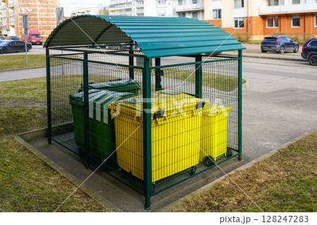 Recycling station with yellow and green bins secured under a metal shelter in a residential area Recycling station with yellow and green bins secured under a metal shelter in a residential area 128247283
