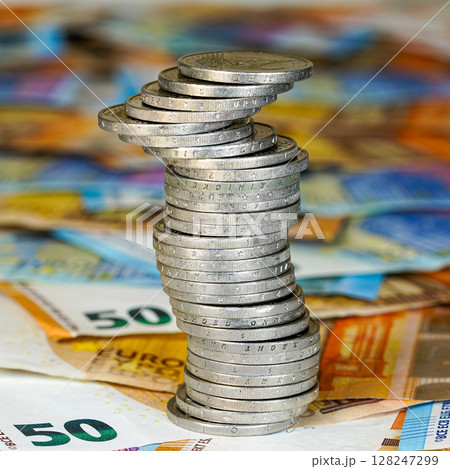 Wobbly stack of euro coins balances on colorful euro banknotes symbolizing wealth and financial risk 128247299