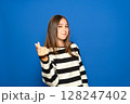 A beautiful Hispanic teenager in her 15s wearing a striped sweater posing isolated against a blue background. Lifestyle concept. Rubbing her fingers together, gesturing for money 128247402