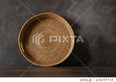 Round woven wicker basket, tray or plate stand on brown background. Asian Style Bamboo basket. Round woven wicker basket, tray or plate stand on brown background. Asian Style Bamboo basket. 128247714