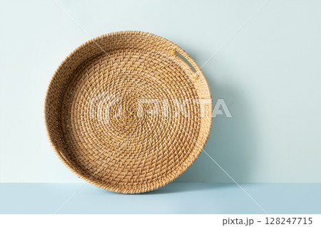 Round woven wicker basket, tray or plate stand on blue background. Handmade by local craftsmen in sri lanka traditional tableware. Round woven wicker basket, tray or plate stand on blue background. Handmade by local craftsmen in sri lanka traditional tableware. 128247715