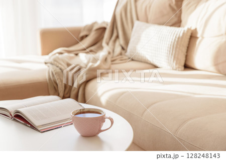 Cozy living room with a book and tea on a beige couch. Soft focus Cozy living room with a book and tea on a beige couch. Soft focus 128248143