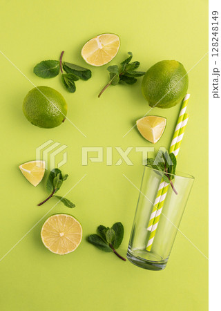 Preparing lemonade. Border from limes, mint leaves, straws, and a glass on a vibrant green background. 128248149