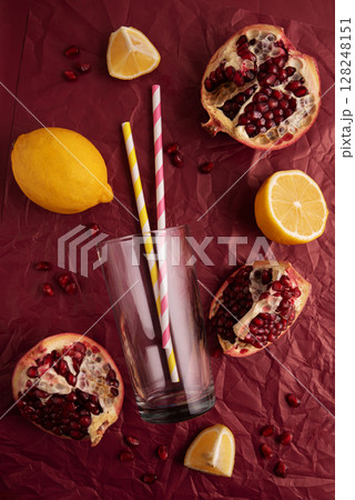 Preparing lemonade. Pomegranates, lemons, straws, and a glass on a red background. 128248151
