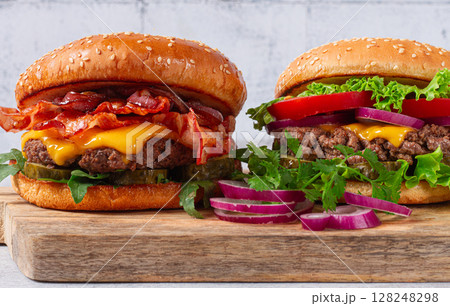 two burgers with beef patty, fried bacon, cheddar cheese, tomatoes, on a light table, two burgers with beef patty, fried bacon, cheddar cheese, tomatoes, on a light table, 128248298