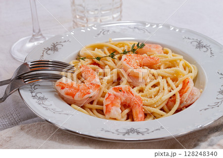 Pasta with shrimp and thyme, served on a white plate, with a glass of white wine, the table is set, there are no people, 128248340