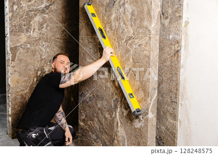 Construction worker using spirit level installing marble tile on wall 128248575