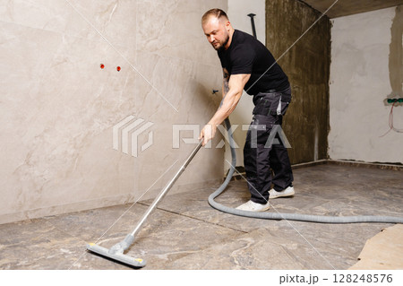 Construction worker vacuuming dust and debris after laying tiles in bathroom Construction worker vacuuming dust and debris after laying tiles in bathroom 128248576