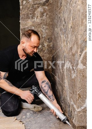 Construction worker applying silicone sealant on tiles in bathroom 128248577