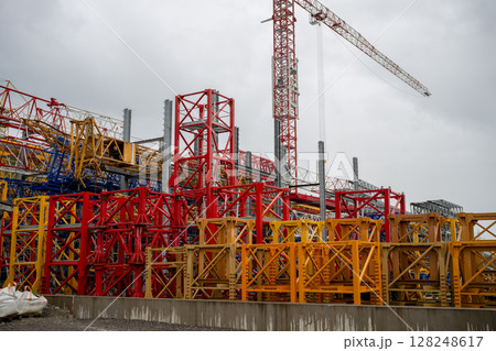 Tall red tower crane and colorful metal structures at construction equipment yard 128248617
