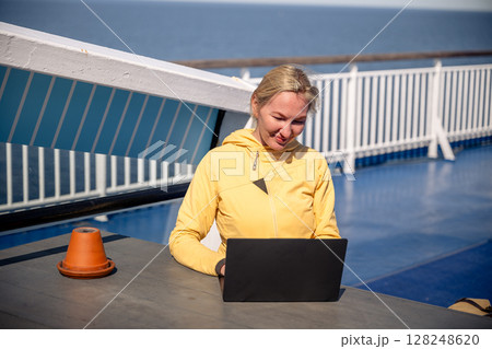 Woman working on laptop outdoors on ferry deck on sunny windy day Woman working on laptop outdoors on ferry deck on sunny windy day 128248620