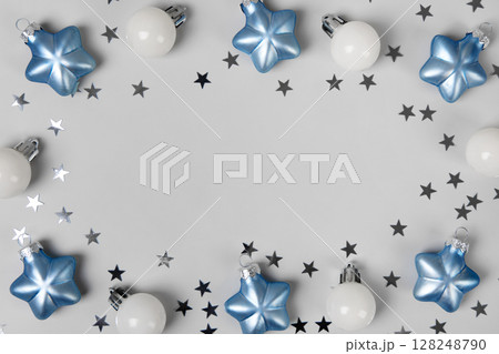 Blue and white Christmas tree balls with silver glitter stars on a gray background with space for text in the center. Christmas and New Year postcard. Flat lay, copy space 128248790
