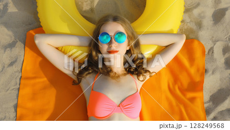Summer vacation, happy relaxing young woman lying on sand on sea beach with swimming inflatable ring 128249568
