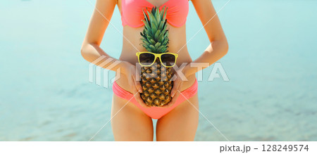 Summer vacation, close up beautiful young woman with pineapple in bikini swimsuit on sea beach Summer vacation, close up beautiful young woman with pineapple in bikini swimsuit on sea beach 128249574