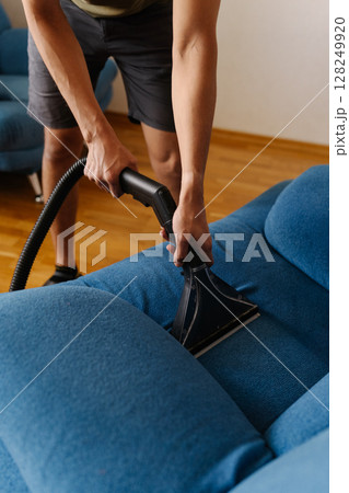 Housekeeper employee vacuuming blue upholstery, removing stubborn dirt and eliminating stains for spotless, sanitized furniture surface closeup. Concept of domestic work, housekeeping, household. 128249920