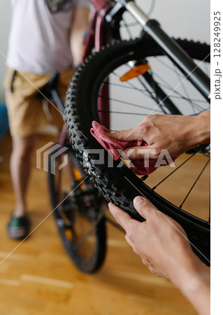 Vertical cropped shot of cyclist cleaning tire of bicycle wheel with cloth, ensuring optimal performance and maintaining bike pristine condition in workshop, close-up. Concept of bike maintenance. 128249925