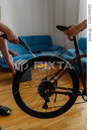 Two people cleaning bicycle wheel with steam cleaner, removing dirt and grime in cozy home environment, ensuring thorough maintenance and hygiene at domestics interior. Concept of bike service. 128249929