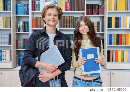 Portrait of two teenage students classmates, smiling guy and girl looking at camera in library 128249961
