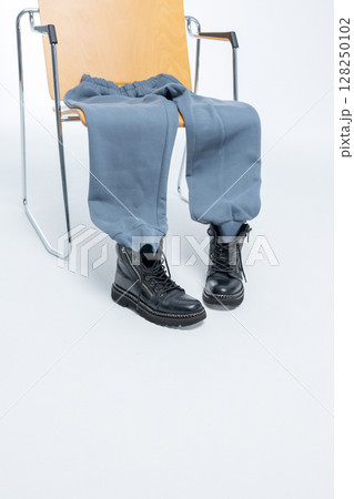 Gray sweatpants with black boots lying on wooden chair on light background. Vertical photo. High quality photo Gray sweatpants with black boots lying on wooden chair on light background. Vertical photo. High quality photo 128250102
