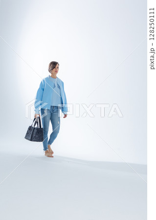 Beautiful woman of model appearance. Girl in blue clothes with black bag on grey background. Pretty female with trendy makeup posing in studio. Vertical photo. High quality photo 128250111
