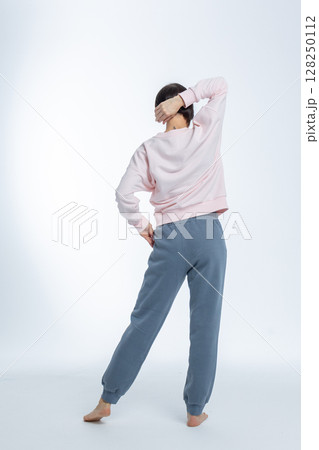 Beautiful woman of model appearance. Girl in light pink jumper and gray trousers on light background. Pretty female with trendy makeup posing in studio. Vertical photo. High quality photo 128250112