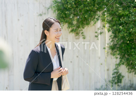 白い塀の前にいるスーツの女性 128254436