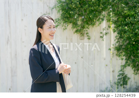 白い塀の前にいるスーツの女性 128254439